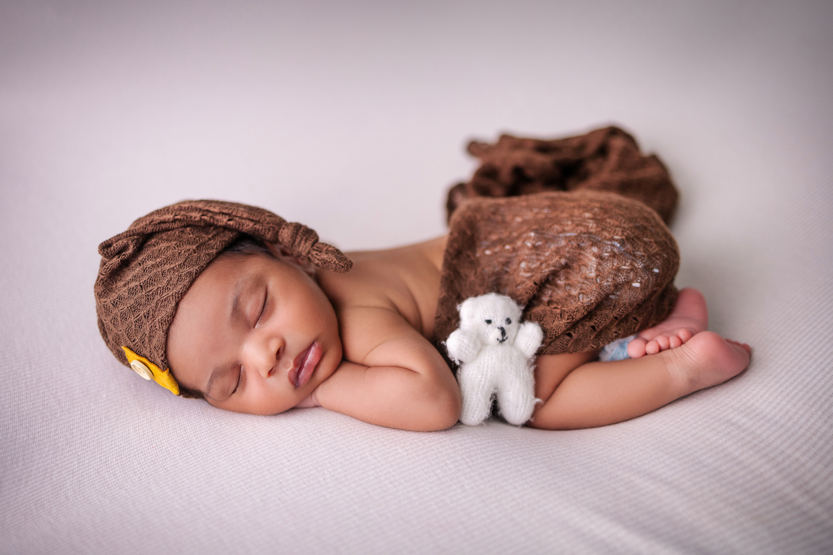 newborn de bruços com lençol, gorro e seu bicho de pelúcia