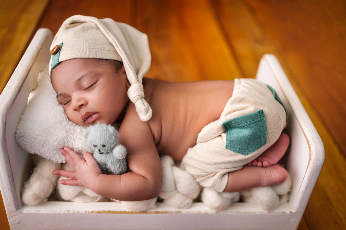 newborn de bruços na props cama com urso de pelúcia