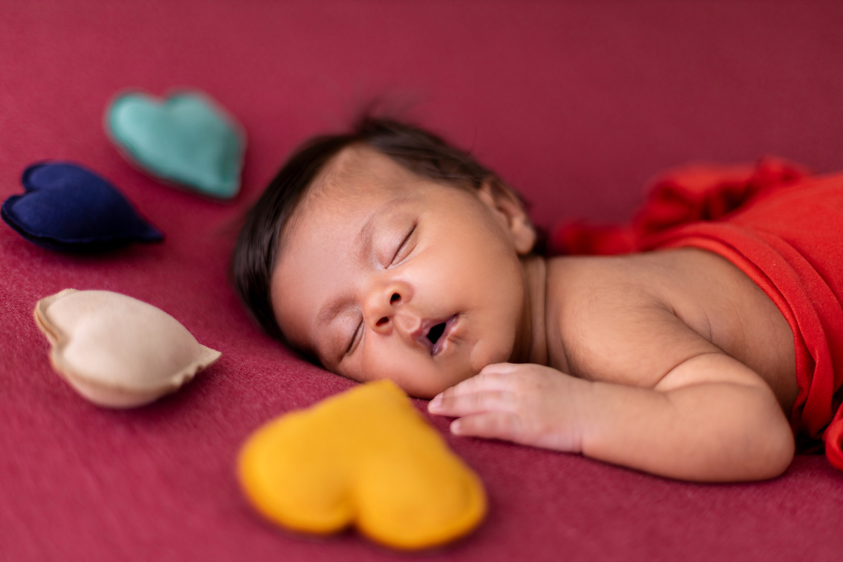 newborn de bruços com lençol e corações