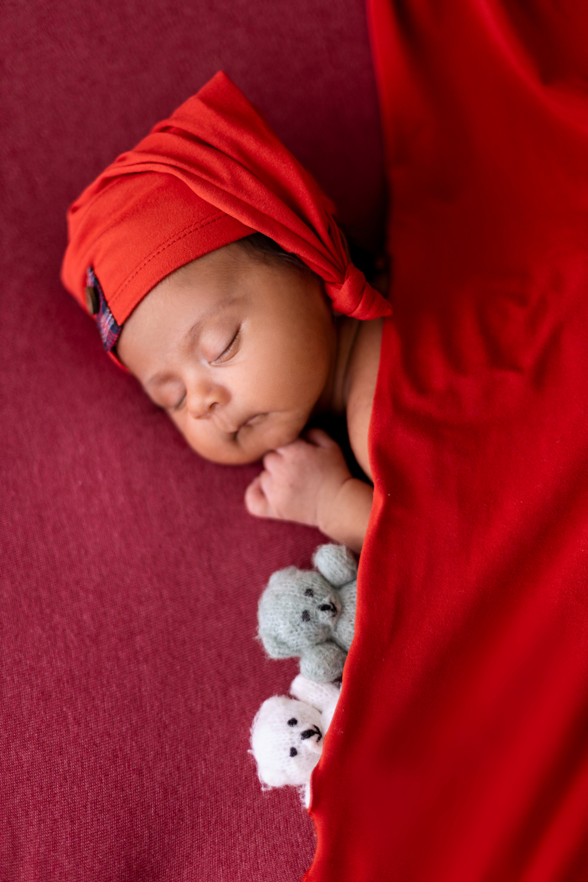 newborn de bruços coberto com gorro e urso de pelúcia
