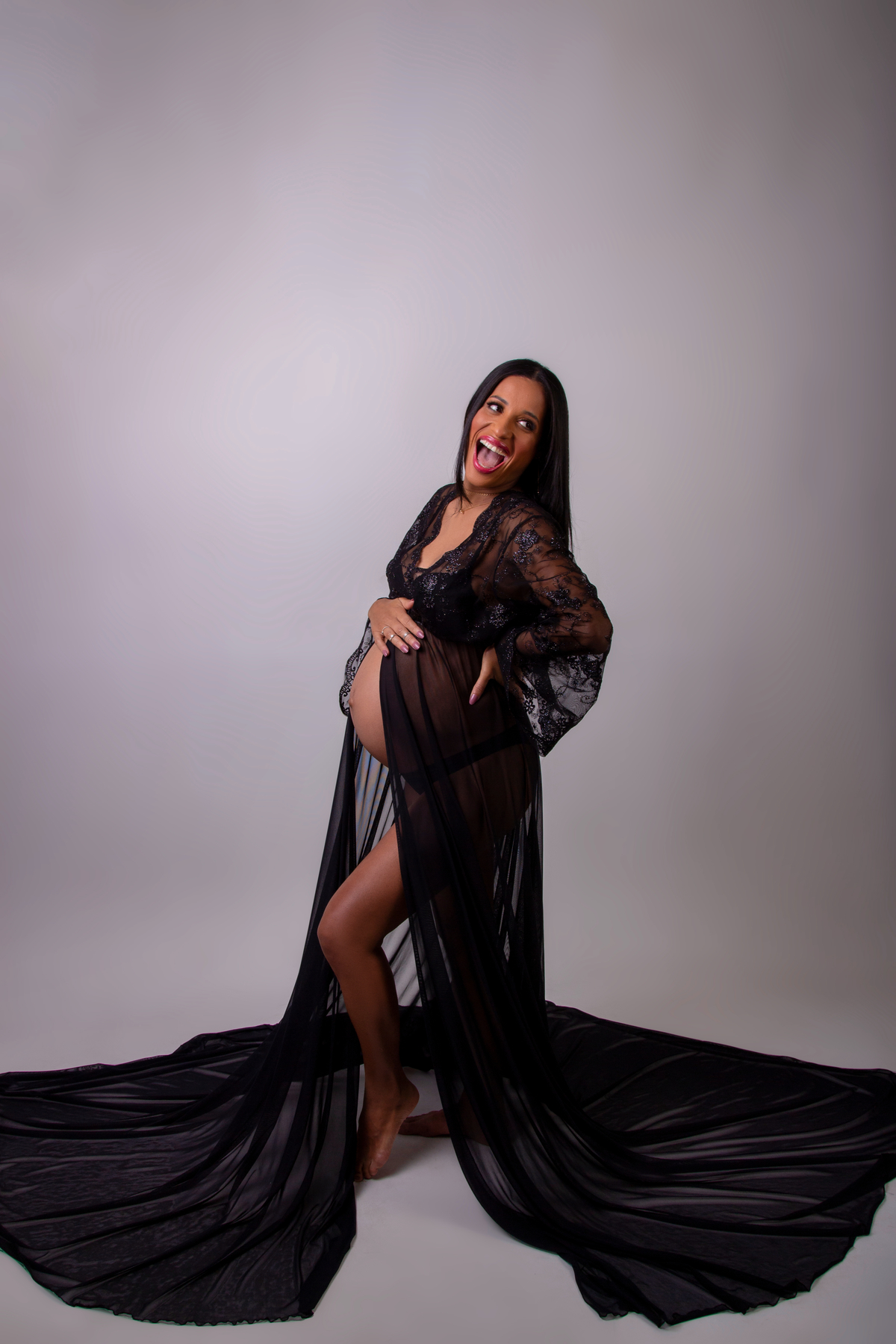 gestante com vestido longo preto com mão na cintura e outra na barriga