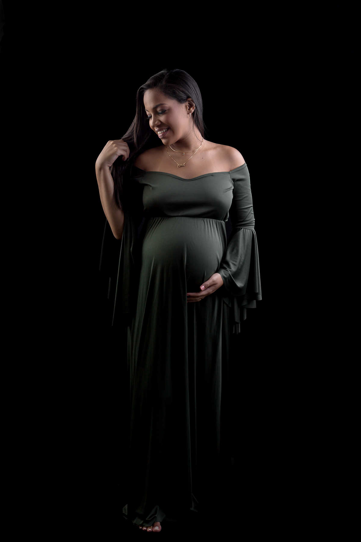 gestante com vestido verde com mão na barriga e outra no cabelo