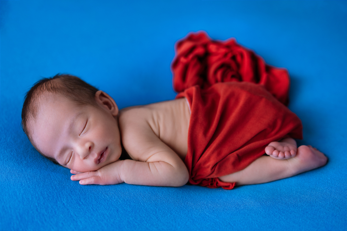 newborn de bruços com lençol vermelho