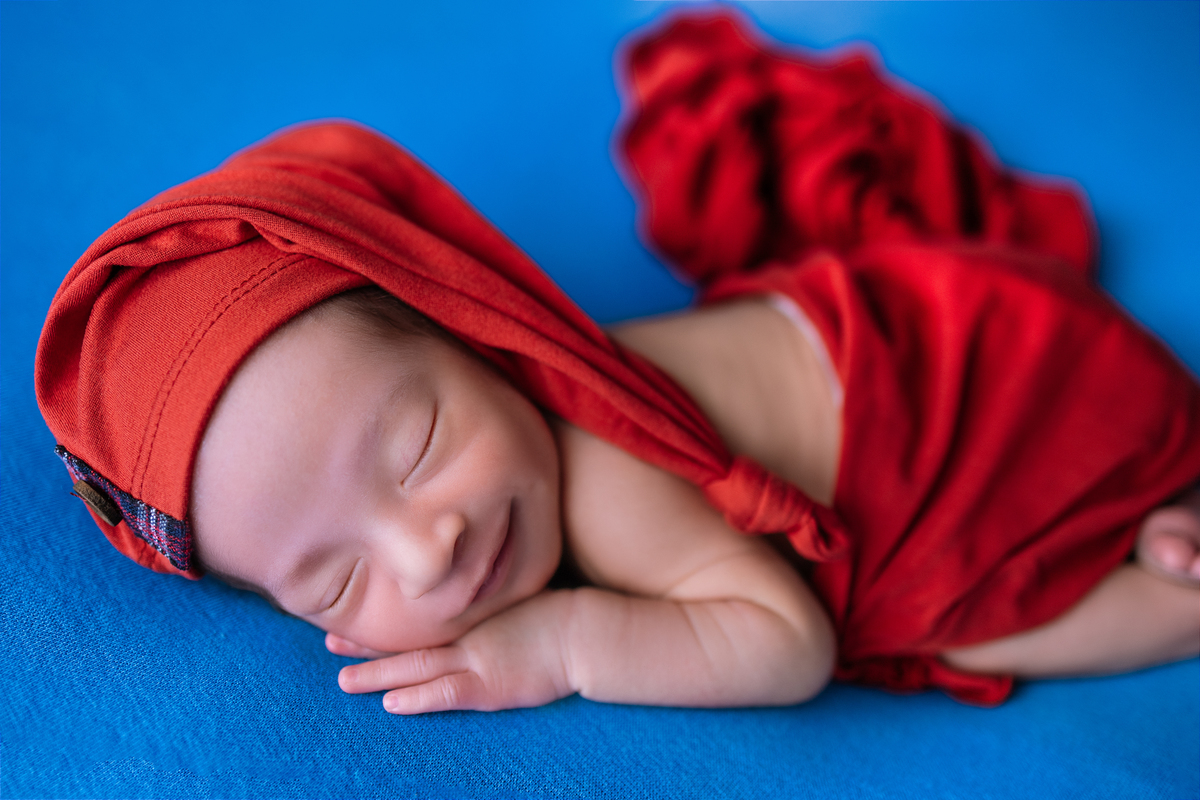 newborn de bruços com lençol e gorro vermelho