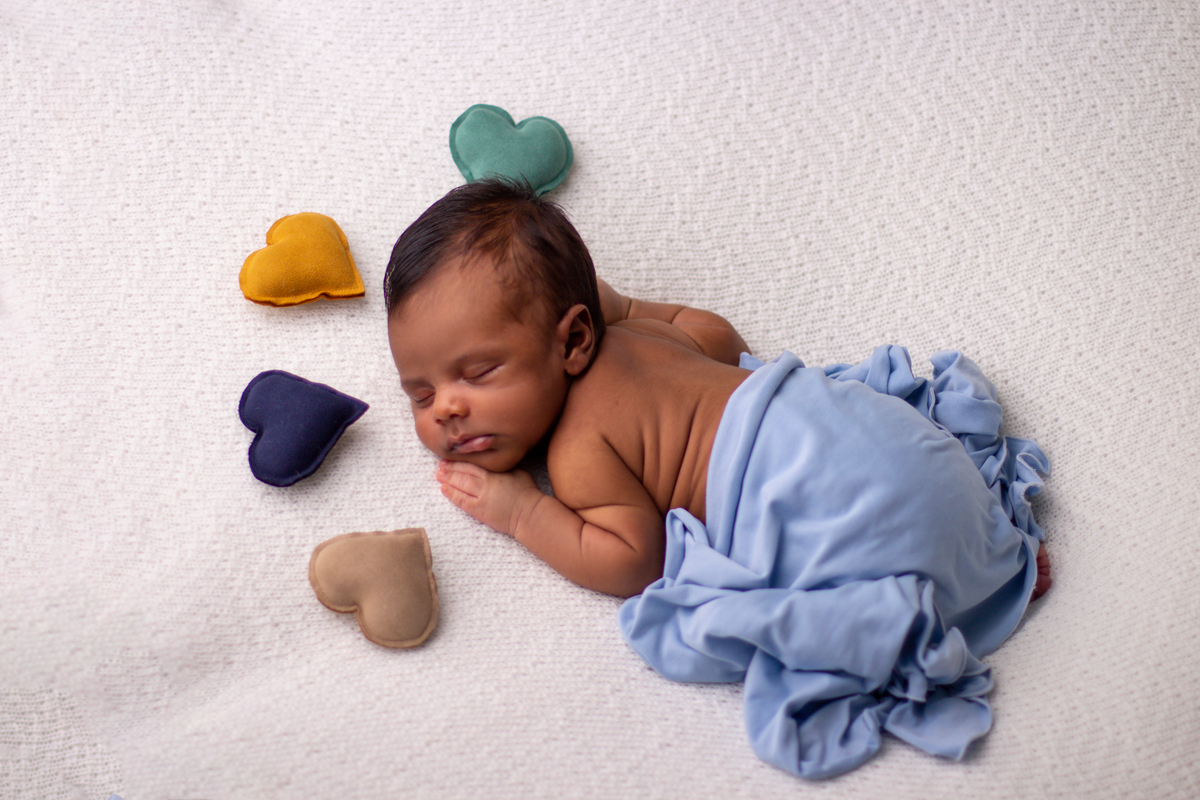newborn de bruços com lençol azul e corações