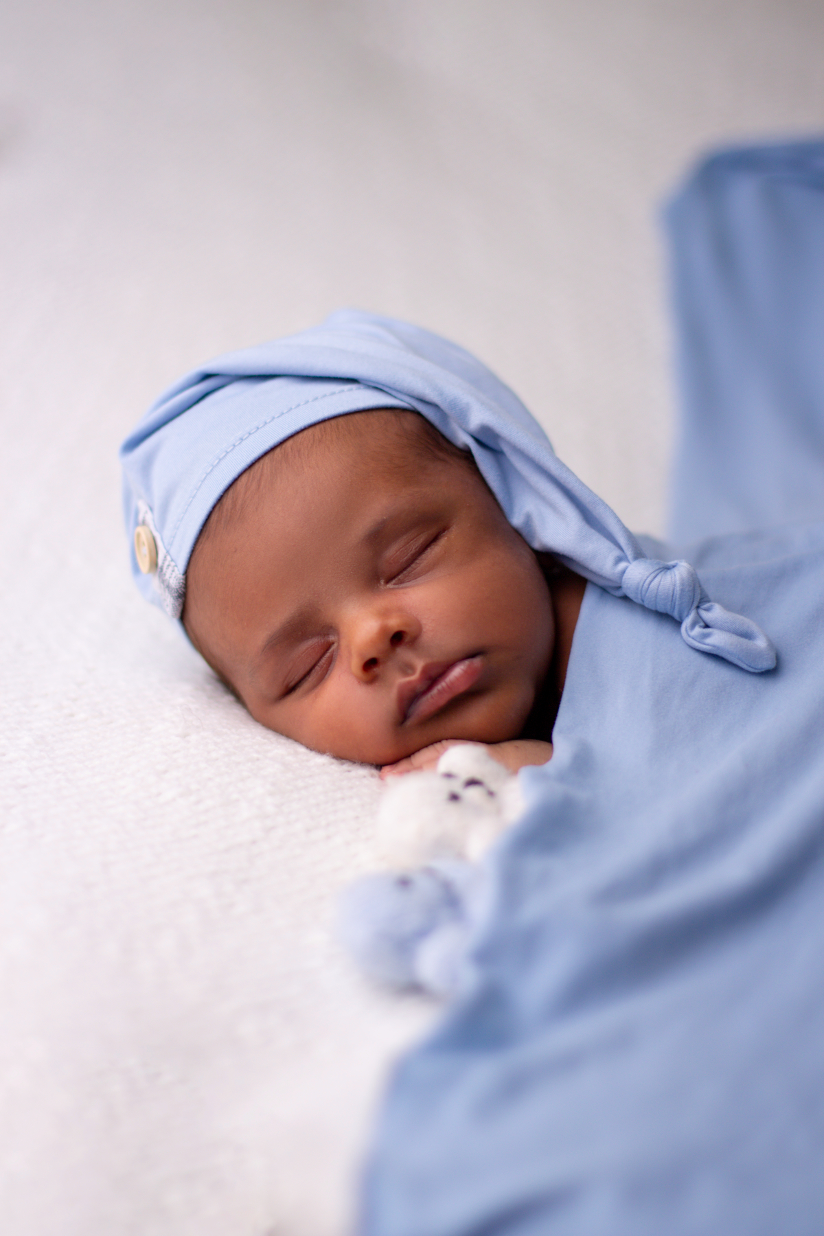 newborn de bruços com lençol azul, gorro e ursinho