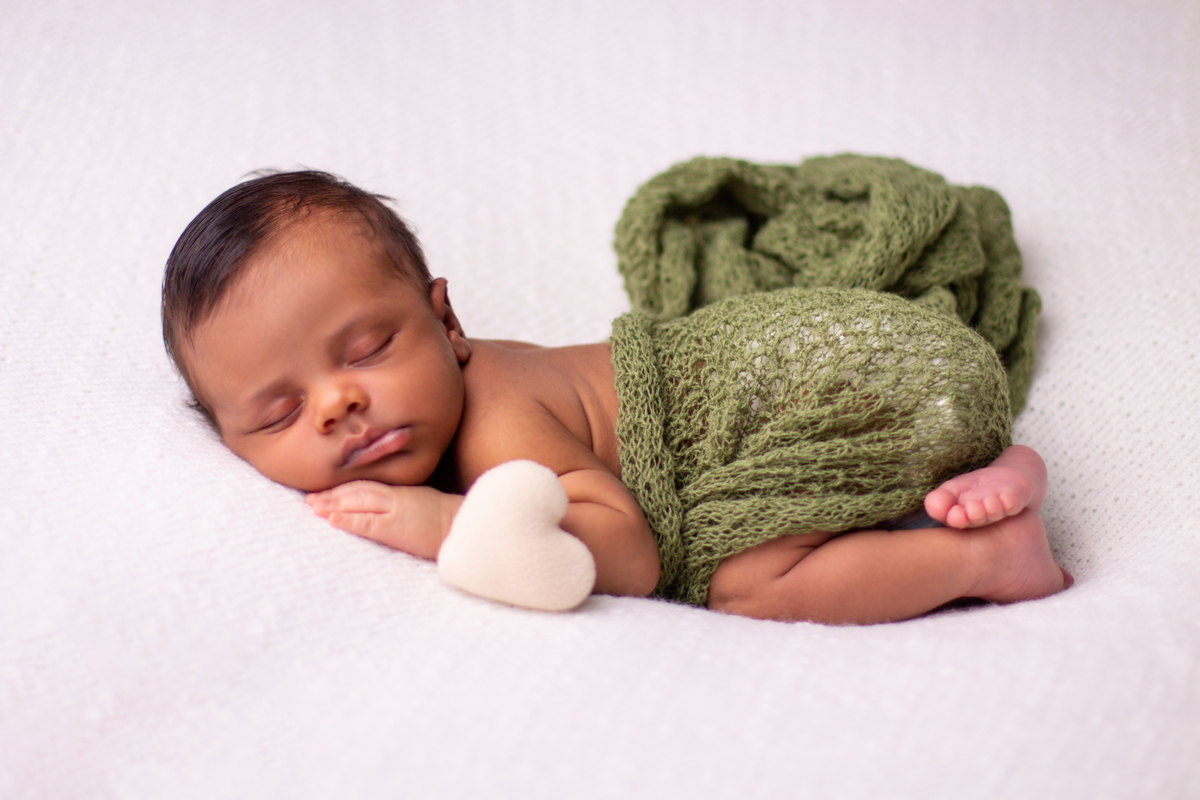 newborn de bruços com lençol verde e coração