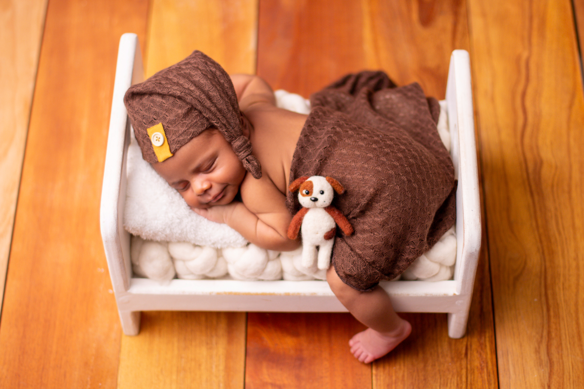 newborn de bruços na props cama com gorro e cachorrinho de pelúcia