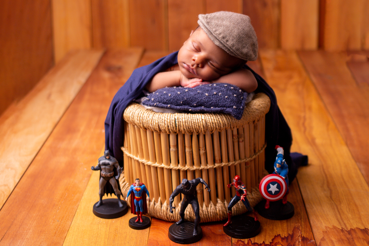 newborn coberto no balde com boina e os brinquedos da Marvel