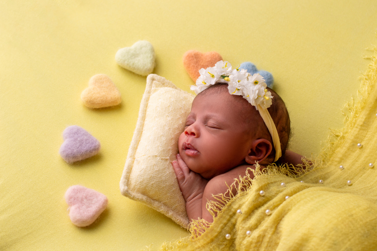newborn deitado de bruços com tiara de flores e corações