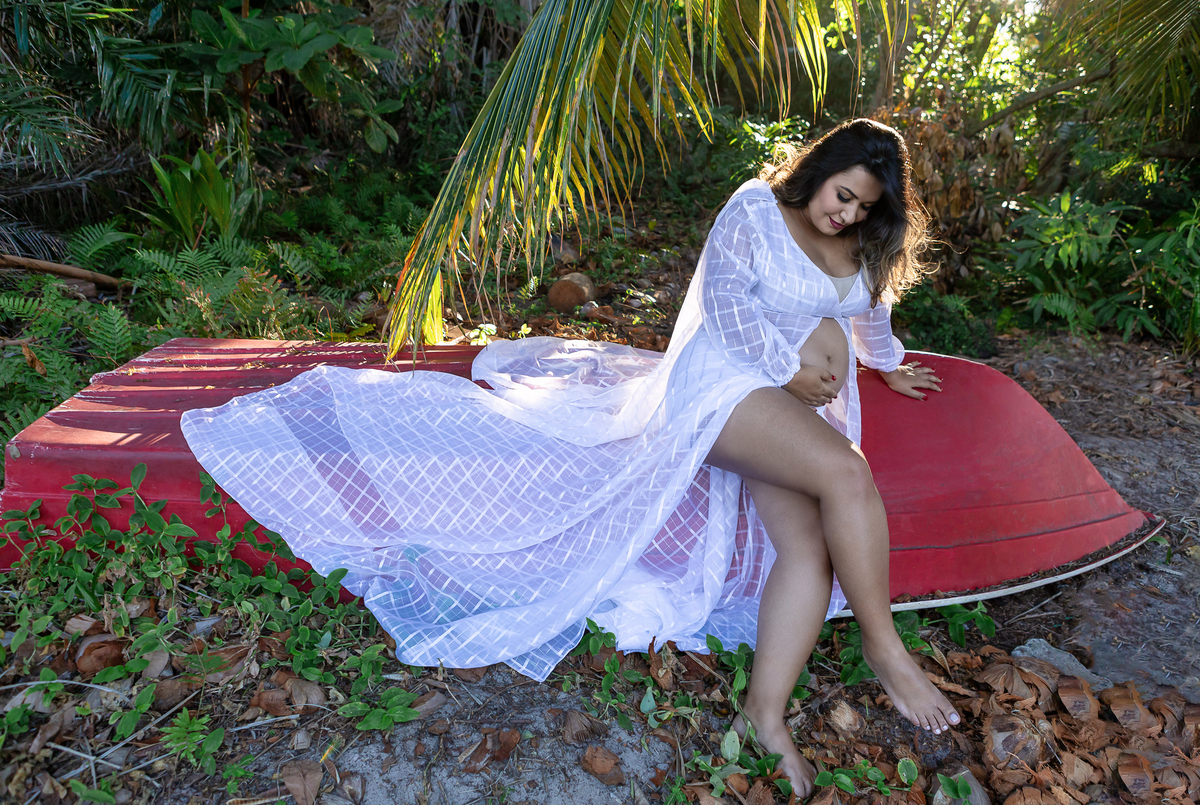 gestante sentada sobre barco virado, e olhando para barriga