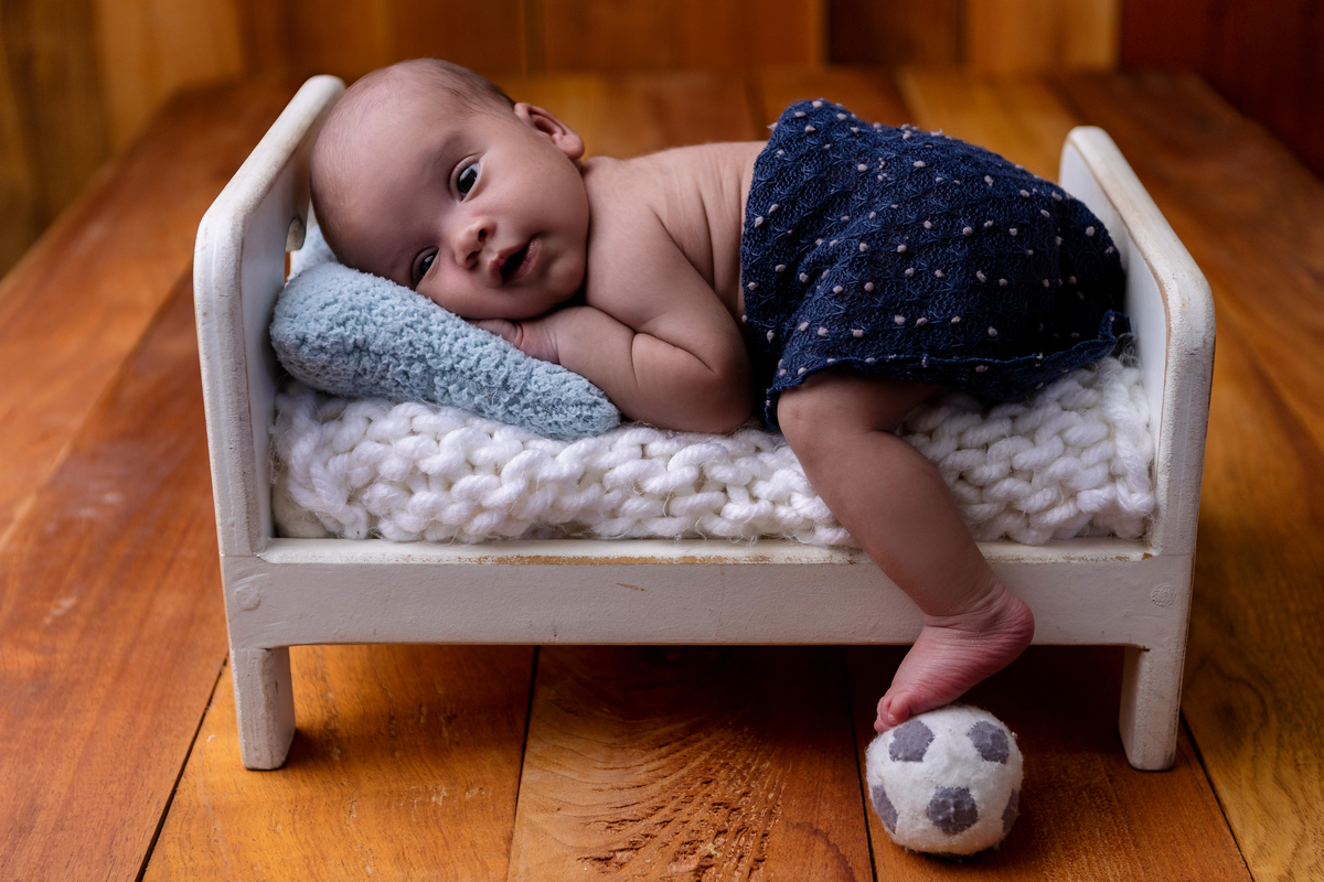 newborn de bruços na props cama segurando a bola de futebol