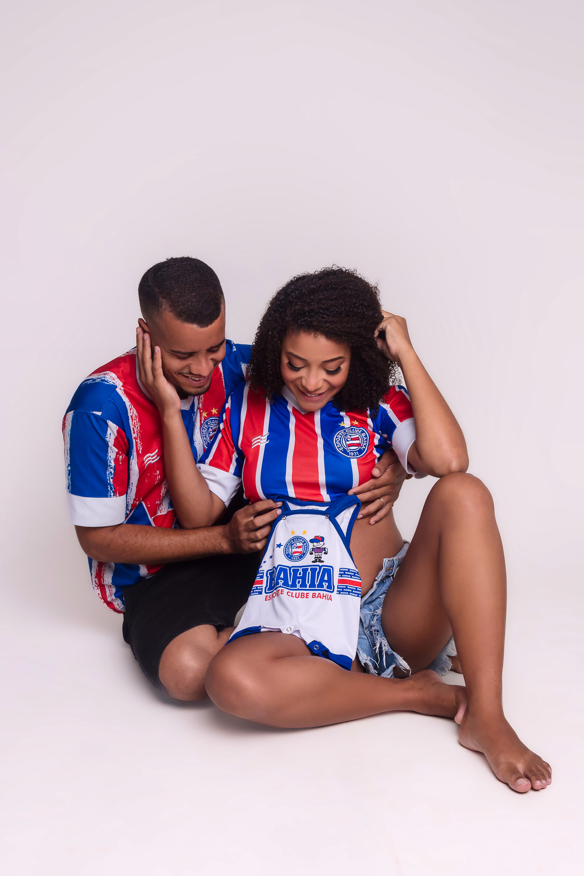 papai e mamãe gestante sentados e olhando pra roupinha do bebê