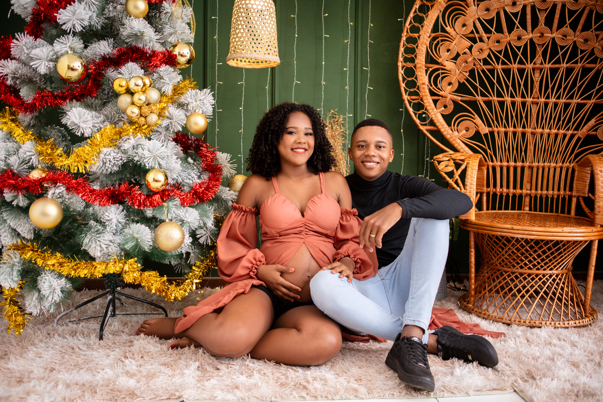 mamãe gestante e papai sentado ao lado da árvore de natal