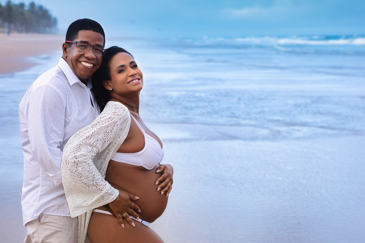 gestante e papai abraçando a barriga na beira do mar