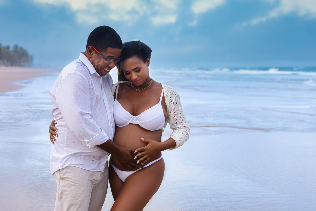 gestante e papai tocando na barriga na beira do mar