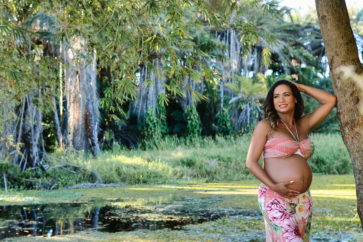 gestante encostada na árvore e tocando na barriga na beira do rio