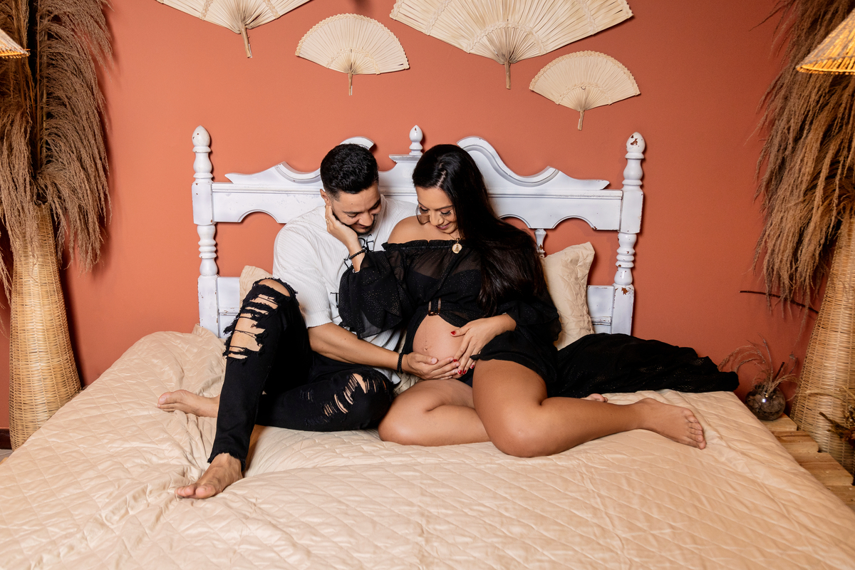 papai e gestante sentados na cama tocando e olhando na barriga