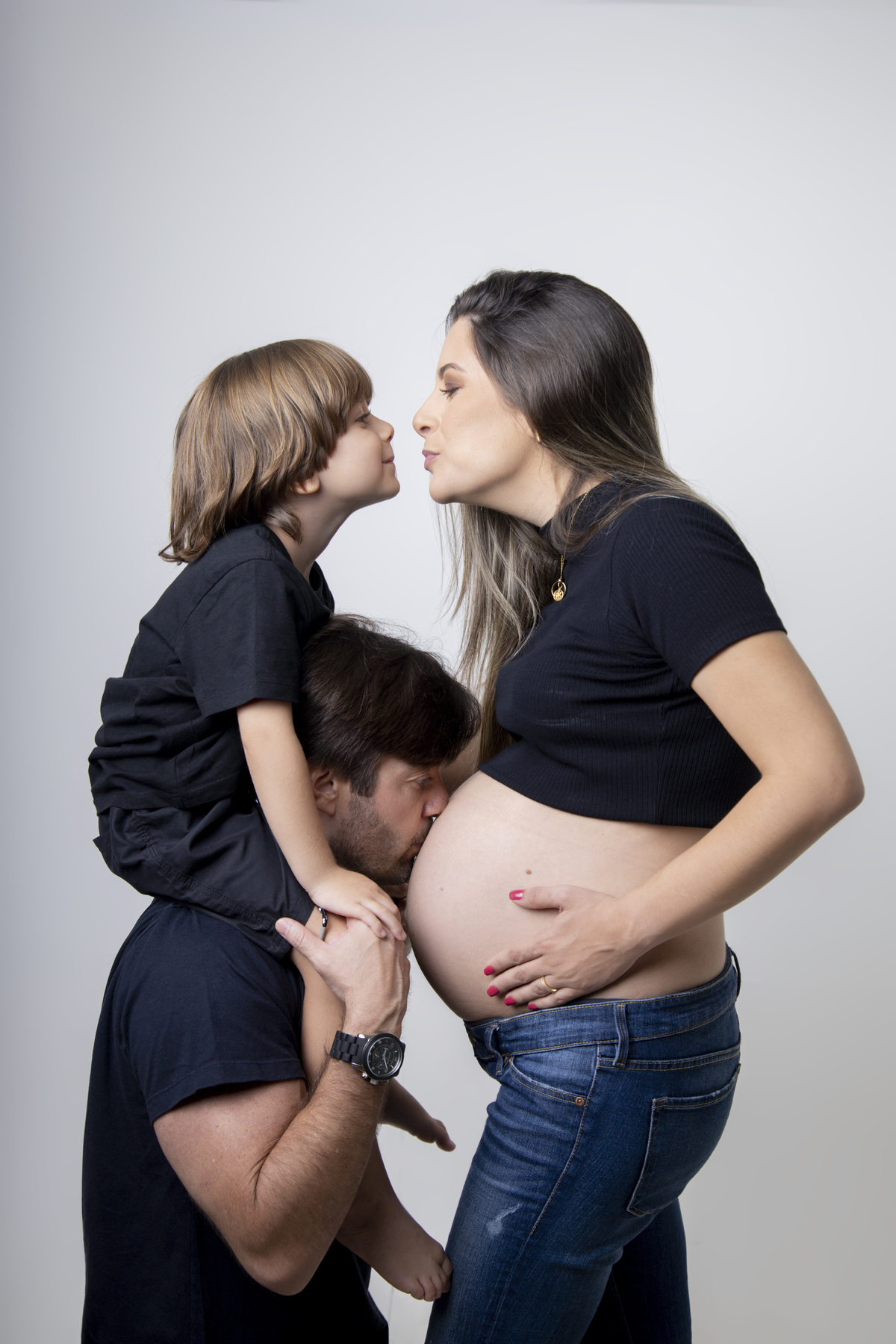 papai ajoelhado com filho no ombro beijando a barriga da gestante