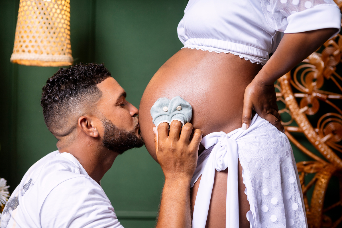 papai com sapatinho do bebê beijando na barriga da gestante