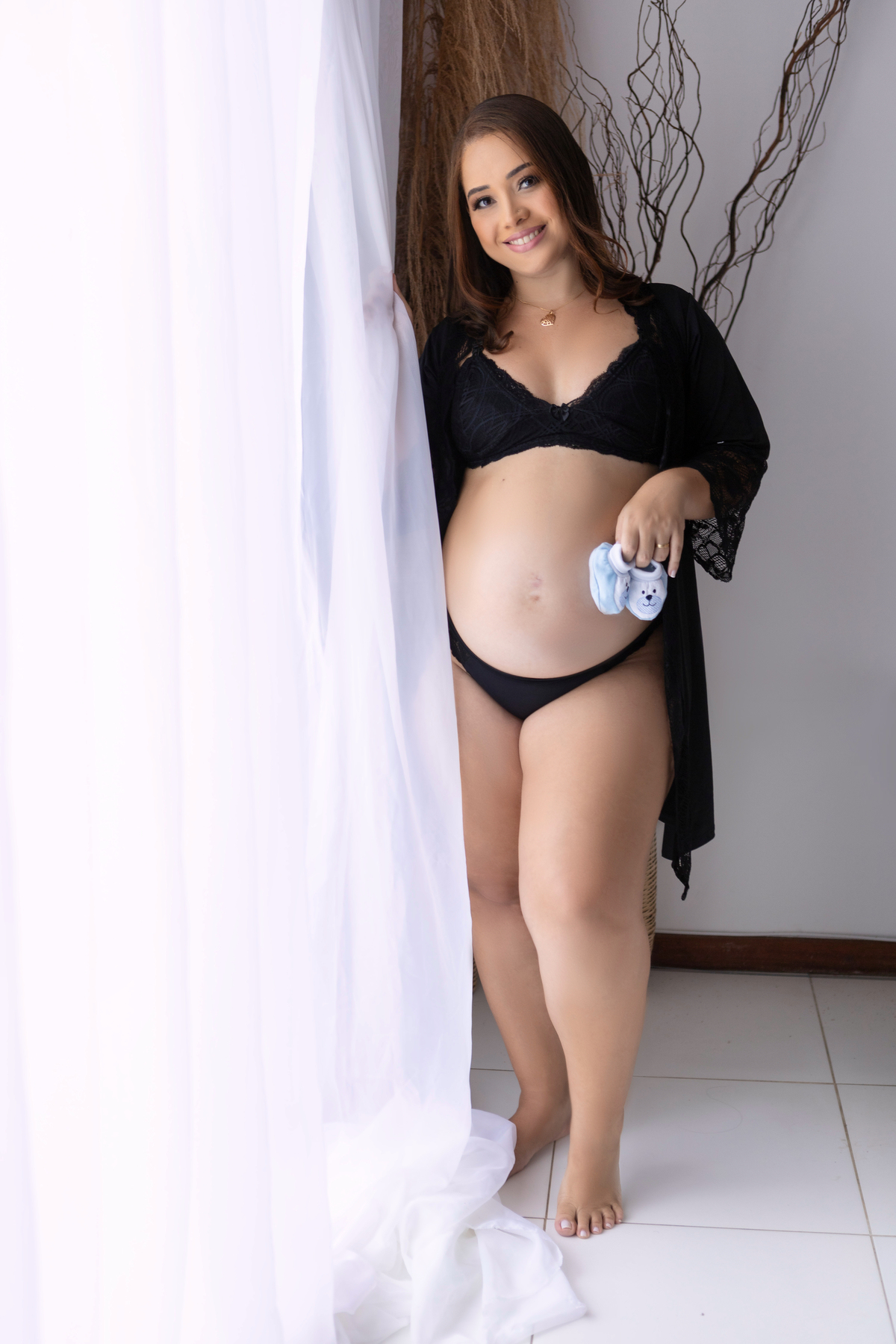 gestante com sapato de bebê e mão na cortina