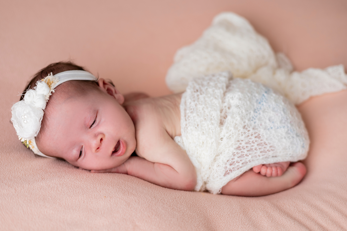  newborn de bruços coberto e com tiara