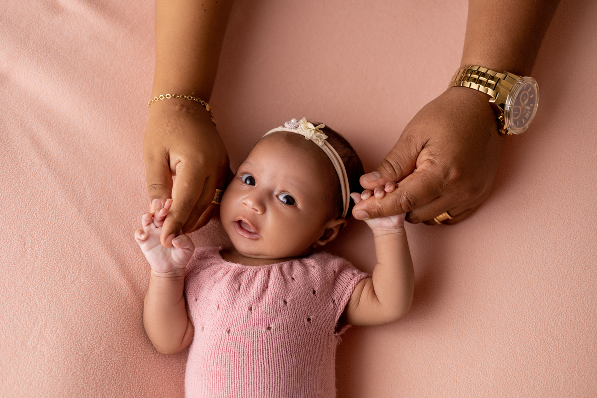 newborn segurando as mãos de seus pais