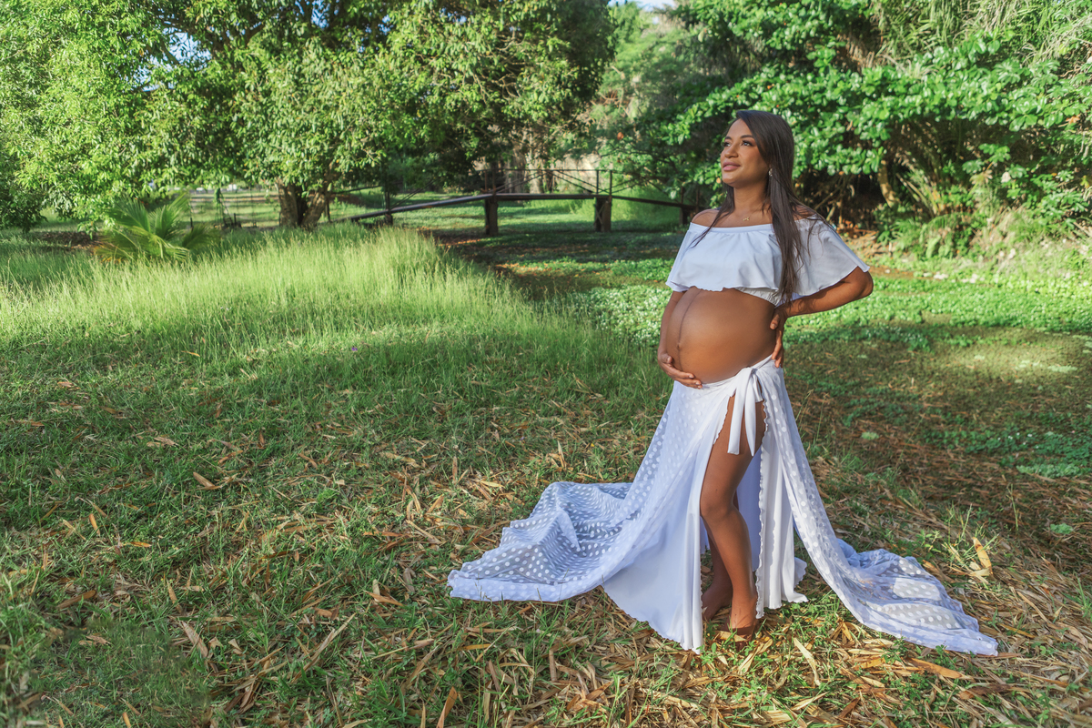 gestante na beira do lago, com mão na cintura e outra na barriga