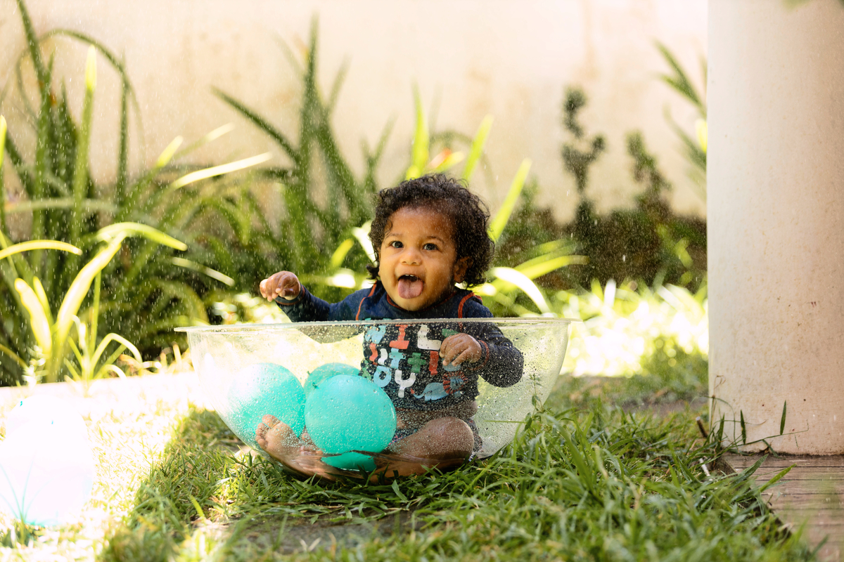 bebê sentado no acrílico brincando com chuva da mangueira