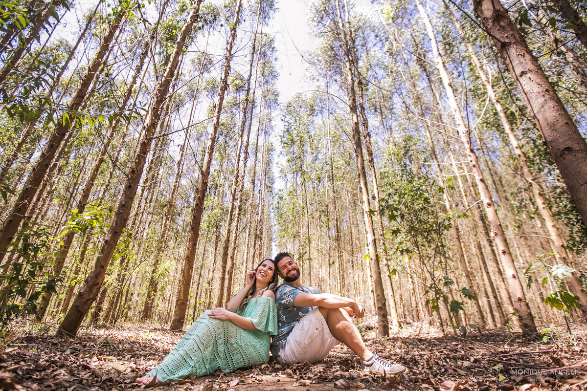 CASAL DE NOIVOS SENTADOS NO CHAO ENTRE EUCALIPTOS DURANTE ENSAIO PRE-WEDDING EM JOAQUIM EGIDIO
