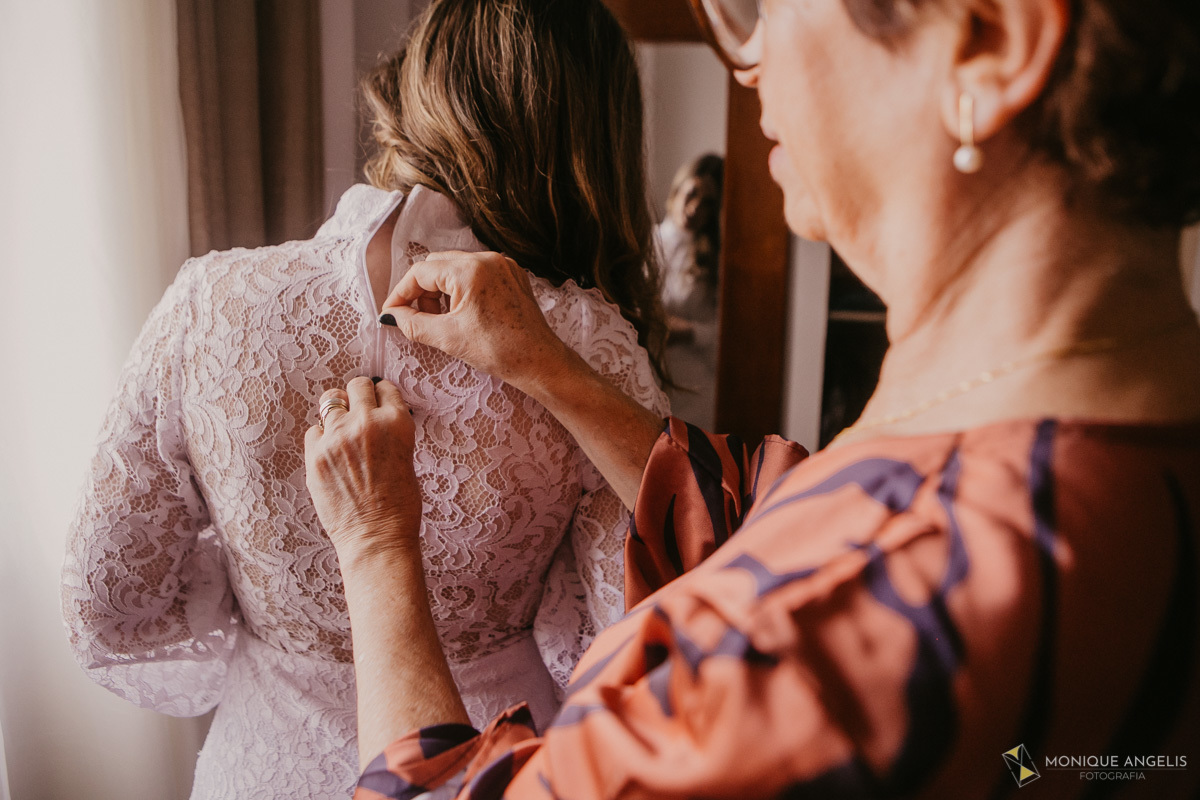 Mãe da noiva fechando o vestido antes da cerimônia de casamento