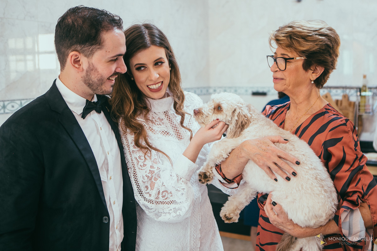 casal de noivos junto com a mãe da noiva brincam com o cachorrinho de estimação