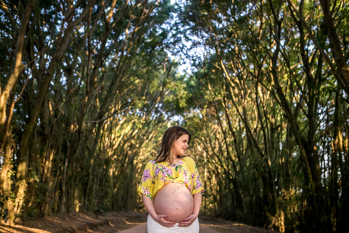 Ensaio Gestante - Gestante em estrada de terra com as mãos na barriga