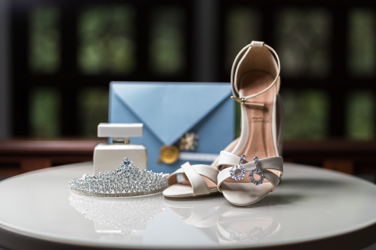 Foto still com adereços da noiva. Convite de casamento, sapato, joias e perfume. Detalhes dos adereços da noiva.