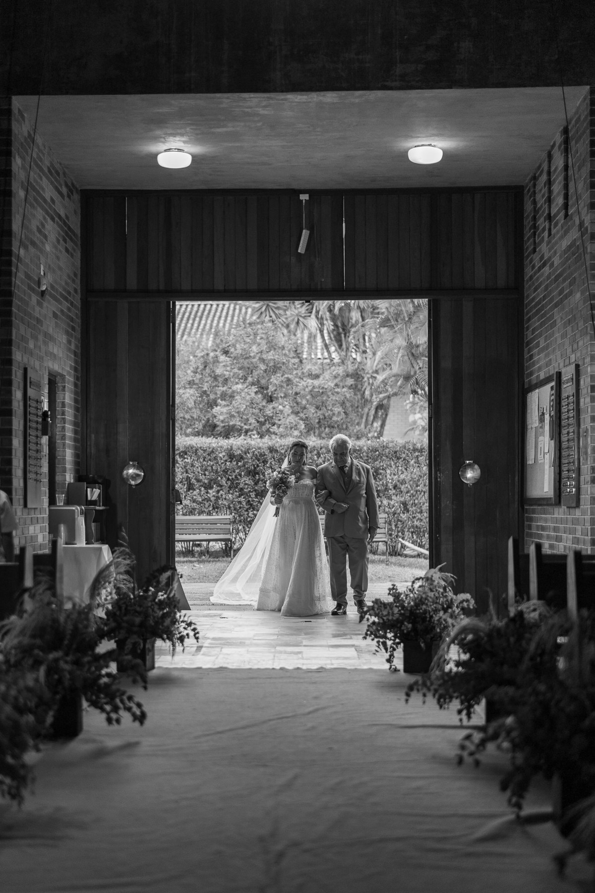 Foto contra luz clássica, de um casamento em capela escandinava, de arquitetura bem caracteristica. Nem mesmo o contra luz é capaz de ofuscar o brilho intenso da noiva entrando na igreja.