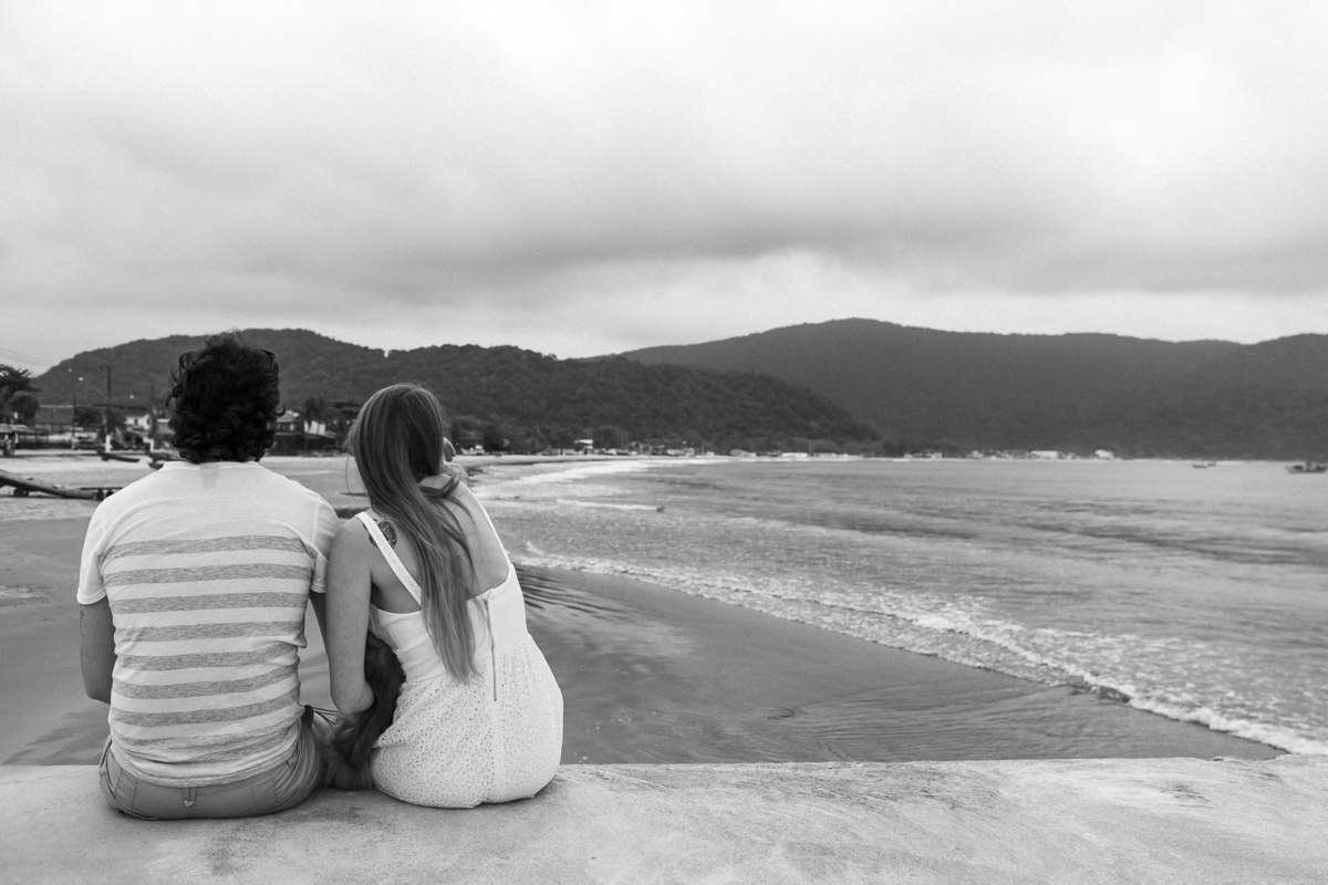 Foto feita na prais onde o casal observa o mar, sentindo a brisa do mar