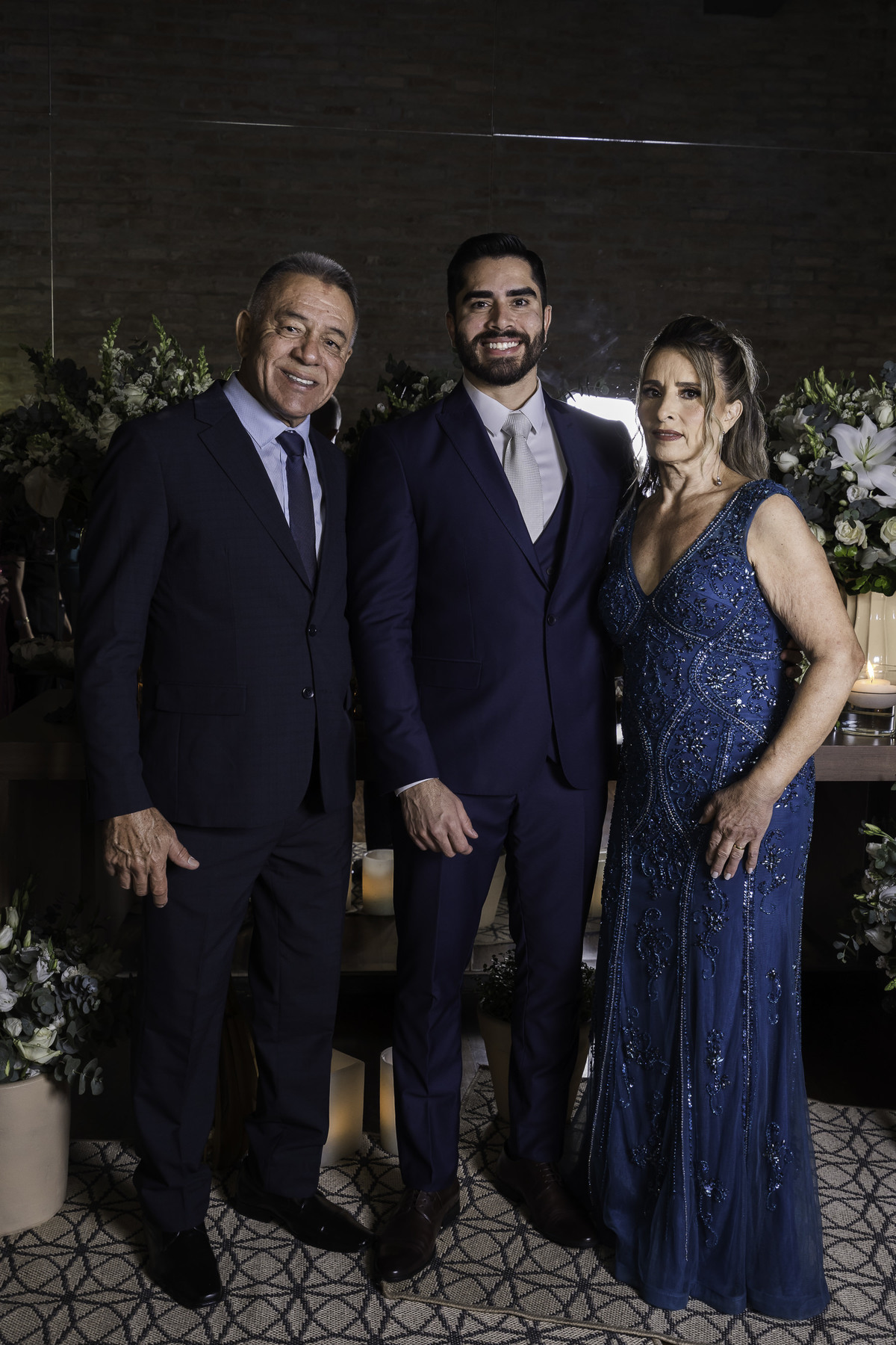 Foto do noivo com os pais, feita em frente a mesa de doces, protocolar de casamento.