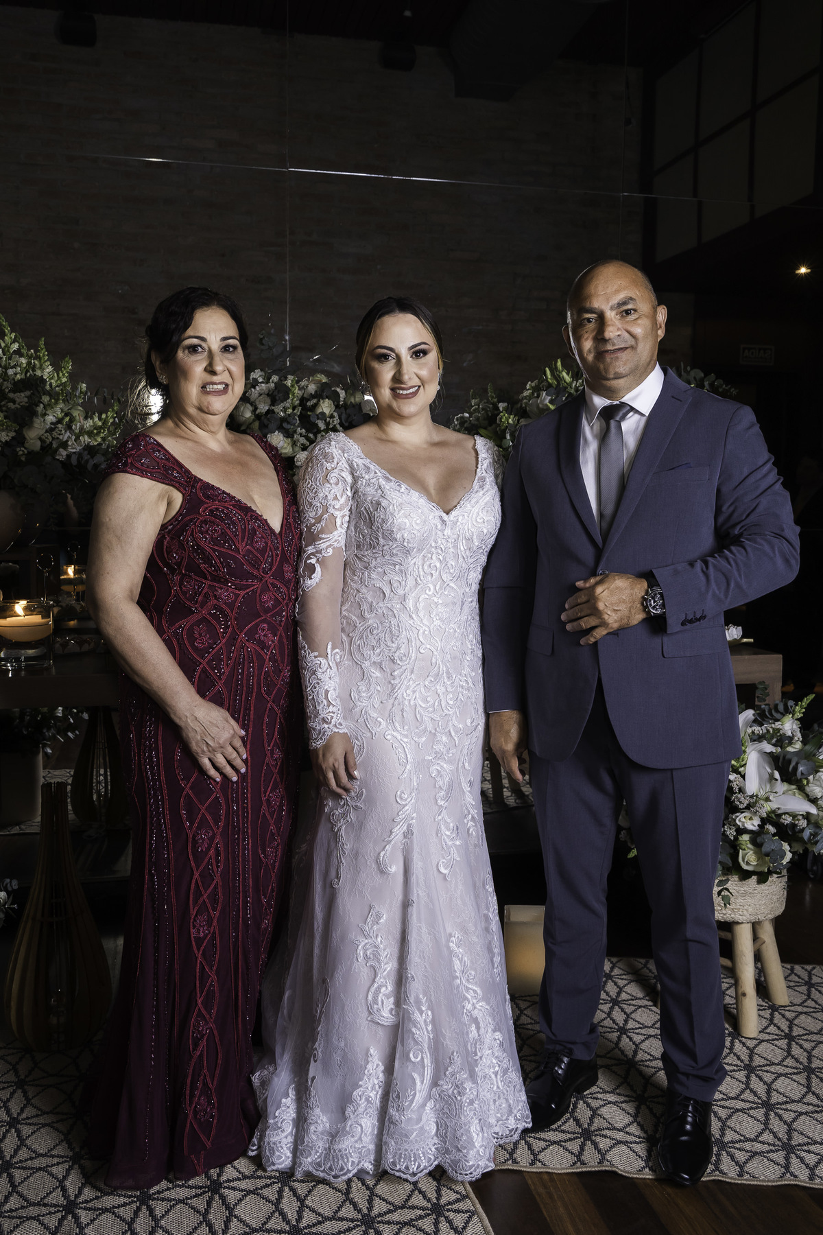 Foto da noiva com os pais, feita em frente a mesa de doces, protocolar de casamento.