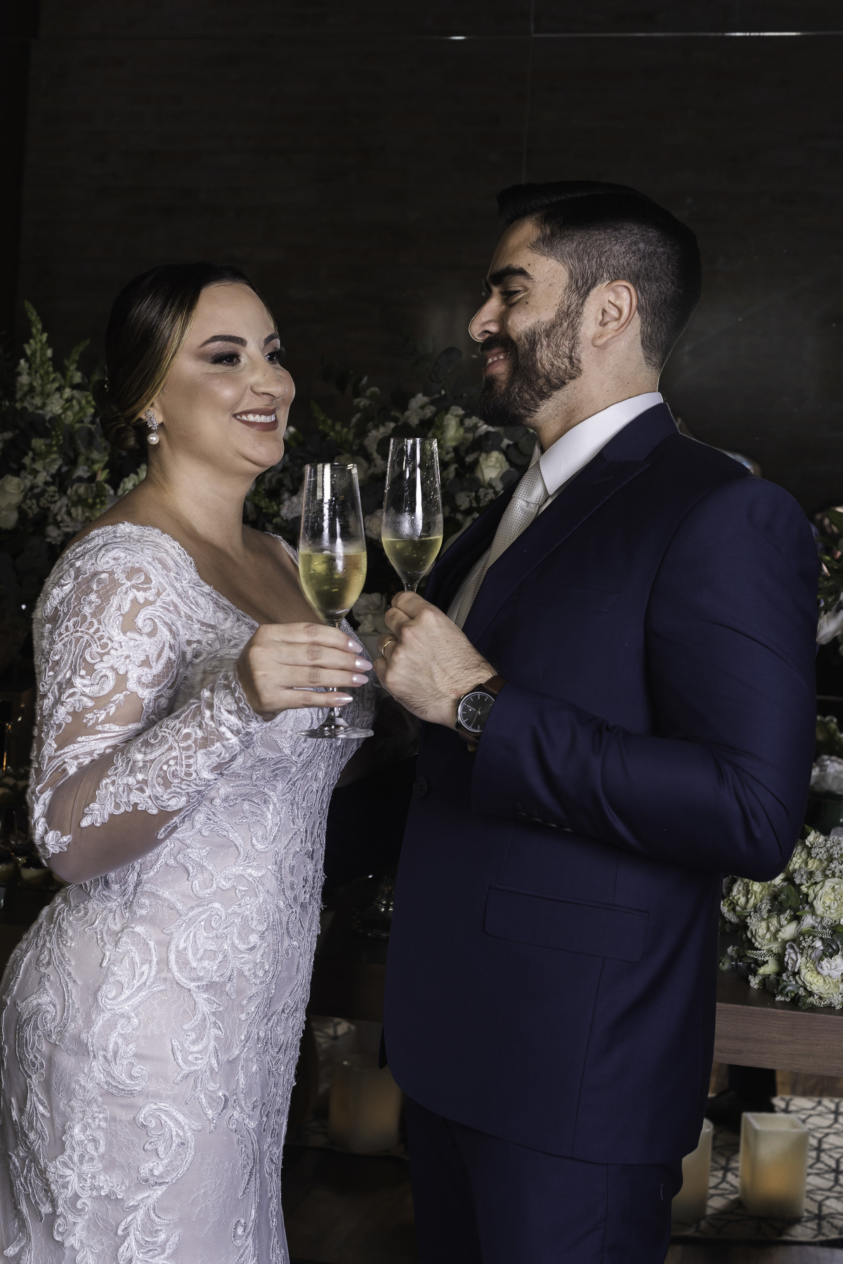 Retrato do casal em frente a mesa de doces, fotoprotocolar e pousada, que mostra o brinde do casal que celebra esta data importante em suas vidas.