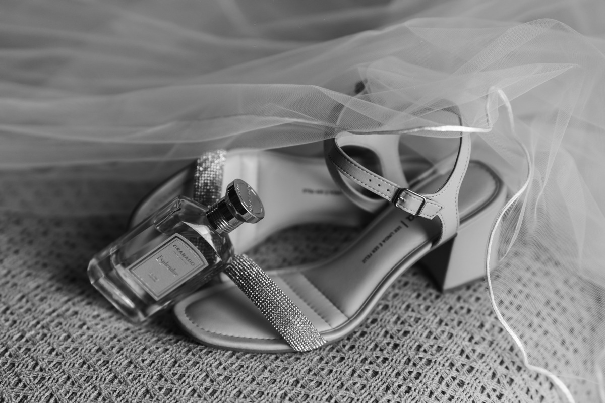 Detalhe do perfume e sandália da noiva, onde a foto se completa com o véu da noiva cercando a composição 