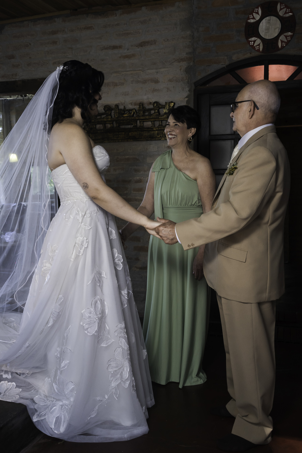 Foto que registrou momento de muito afeto familiar, com os pais da noiva admirando-a vestida de bride.