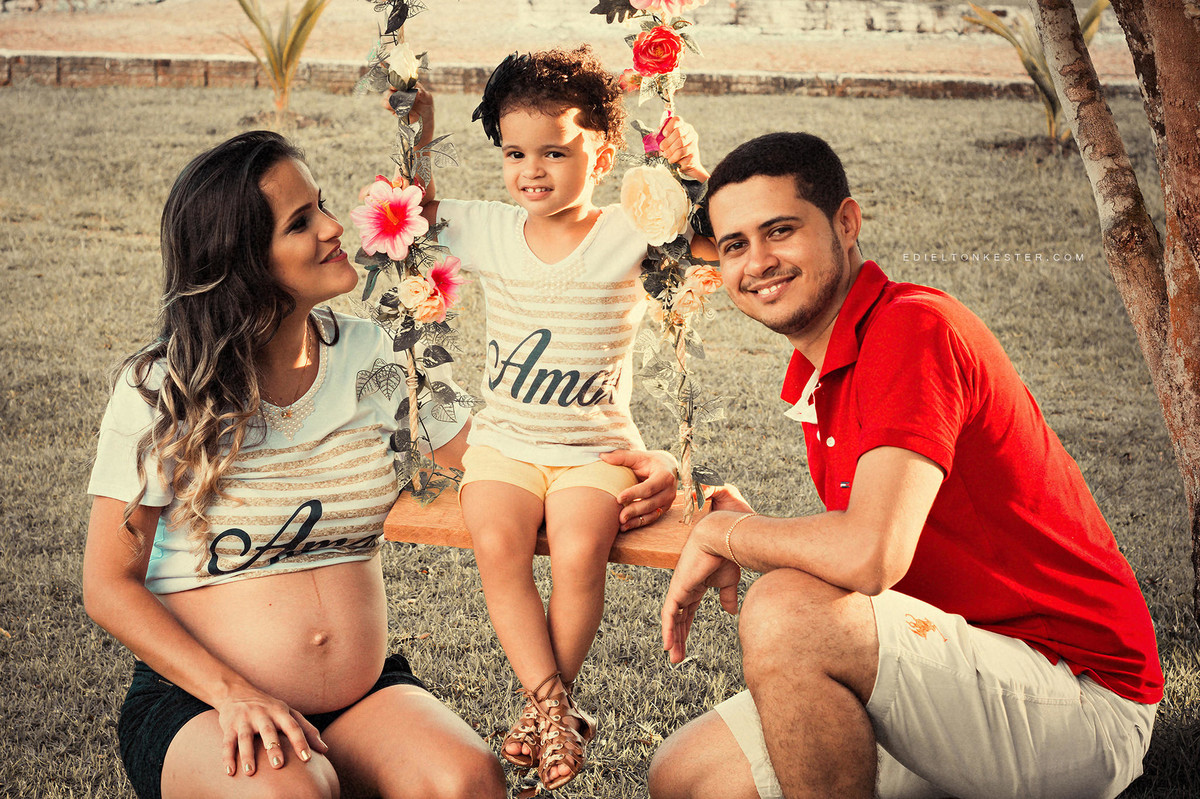 ensaio de gestante com família e filha sentada em balanço de flores