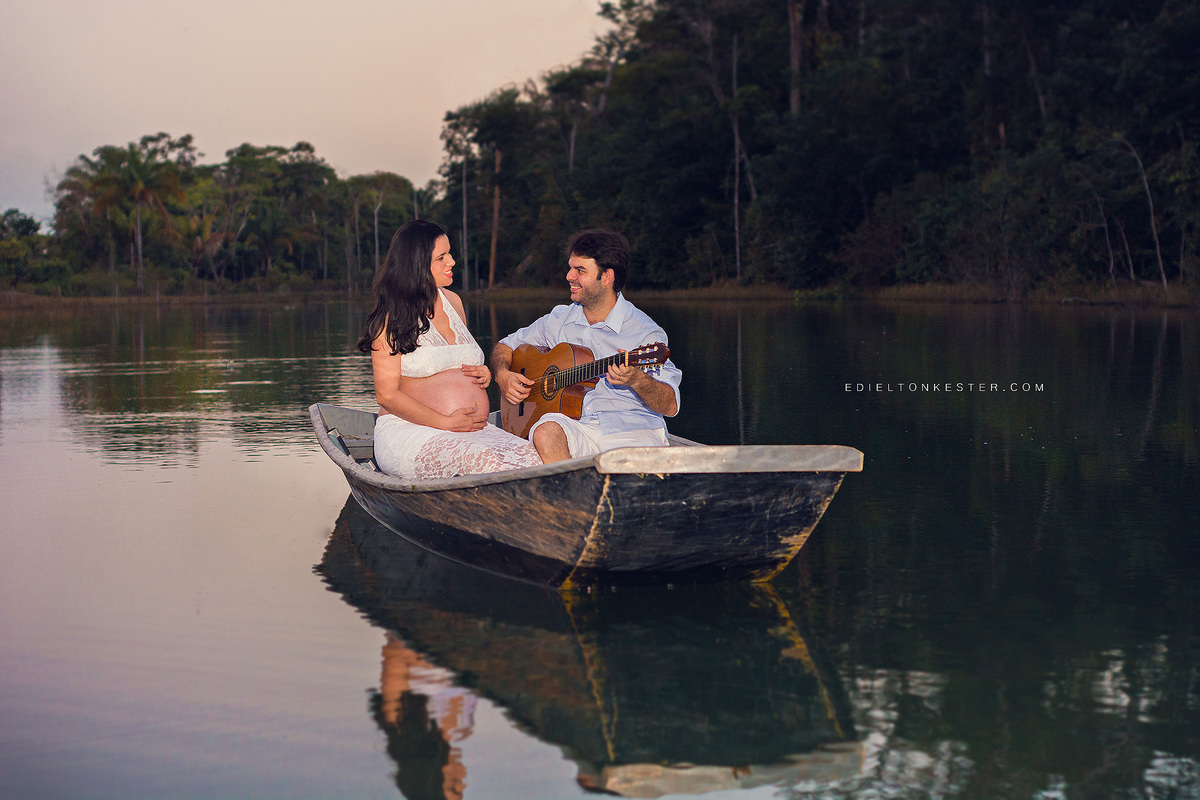 gestante em ensaio externo em barco no meio de um lago com esposo tocando violao 