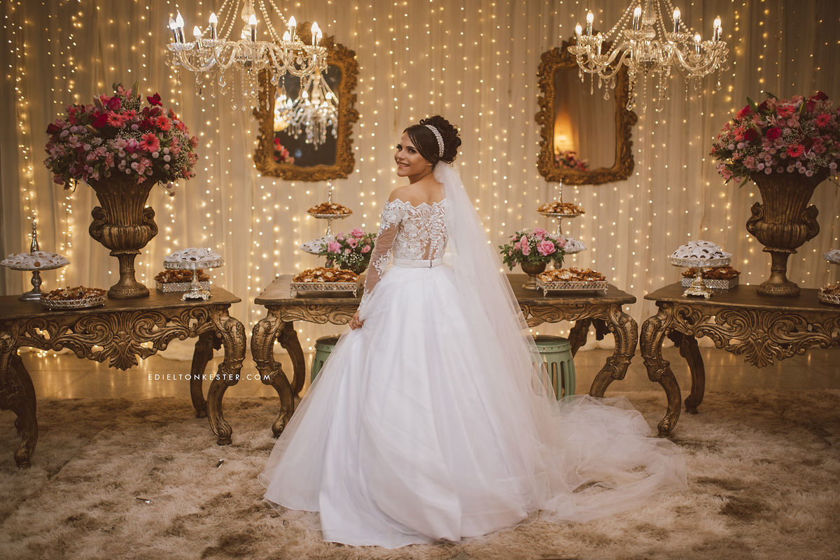 noiva de costas mostrando seu lindo vestido e véu grande em frente a mesa de doces em seu casamento em ji parná