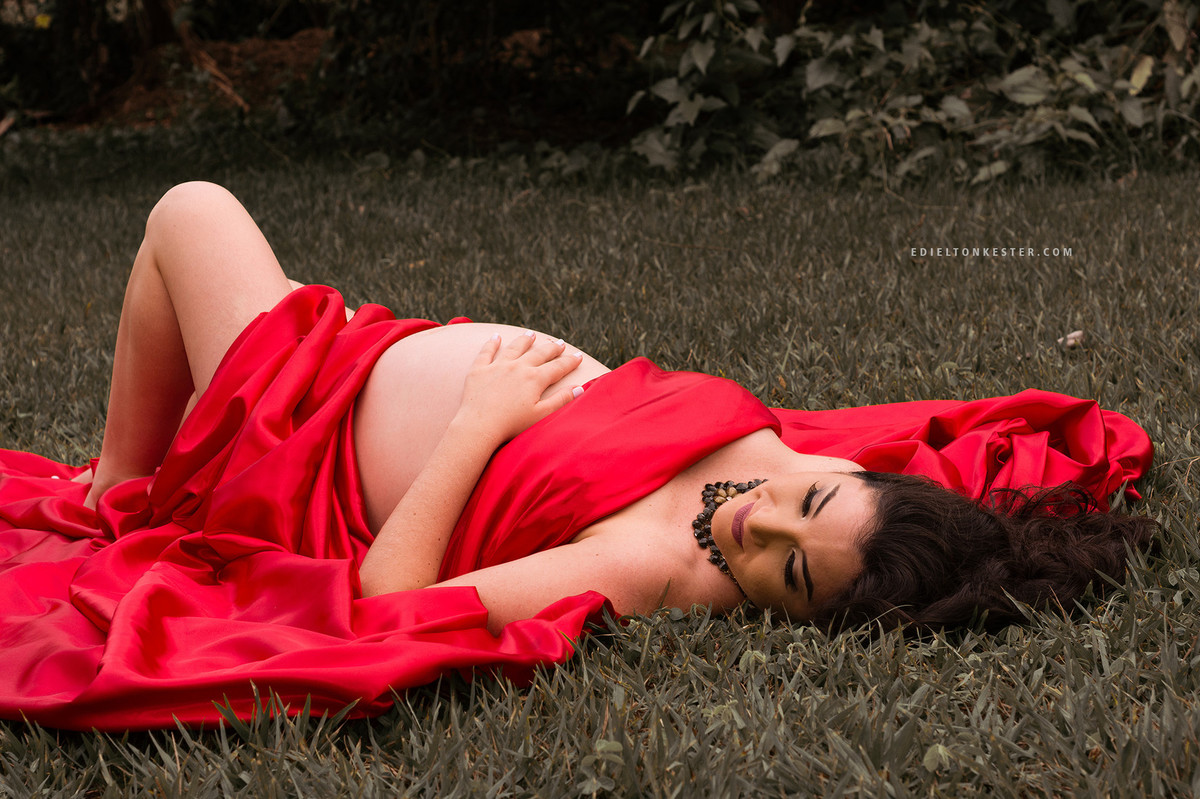 gravida deitada com a mao na barriga e enrolada em tecido vermelho