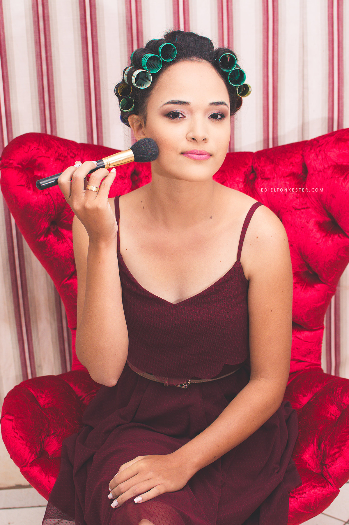 noiva sentada em poltrona e se maquiando em salao no dia do casamento em making of