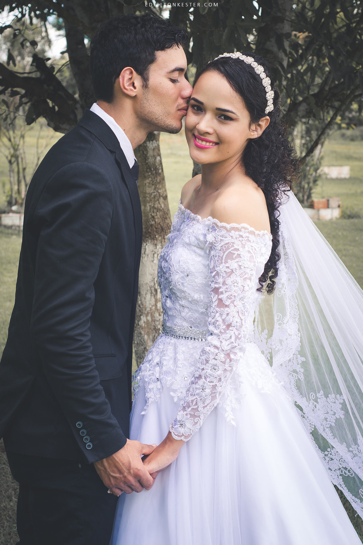 noivo dando um beijo na bochecha da noiva que sorri