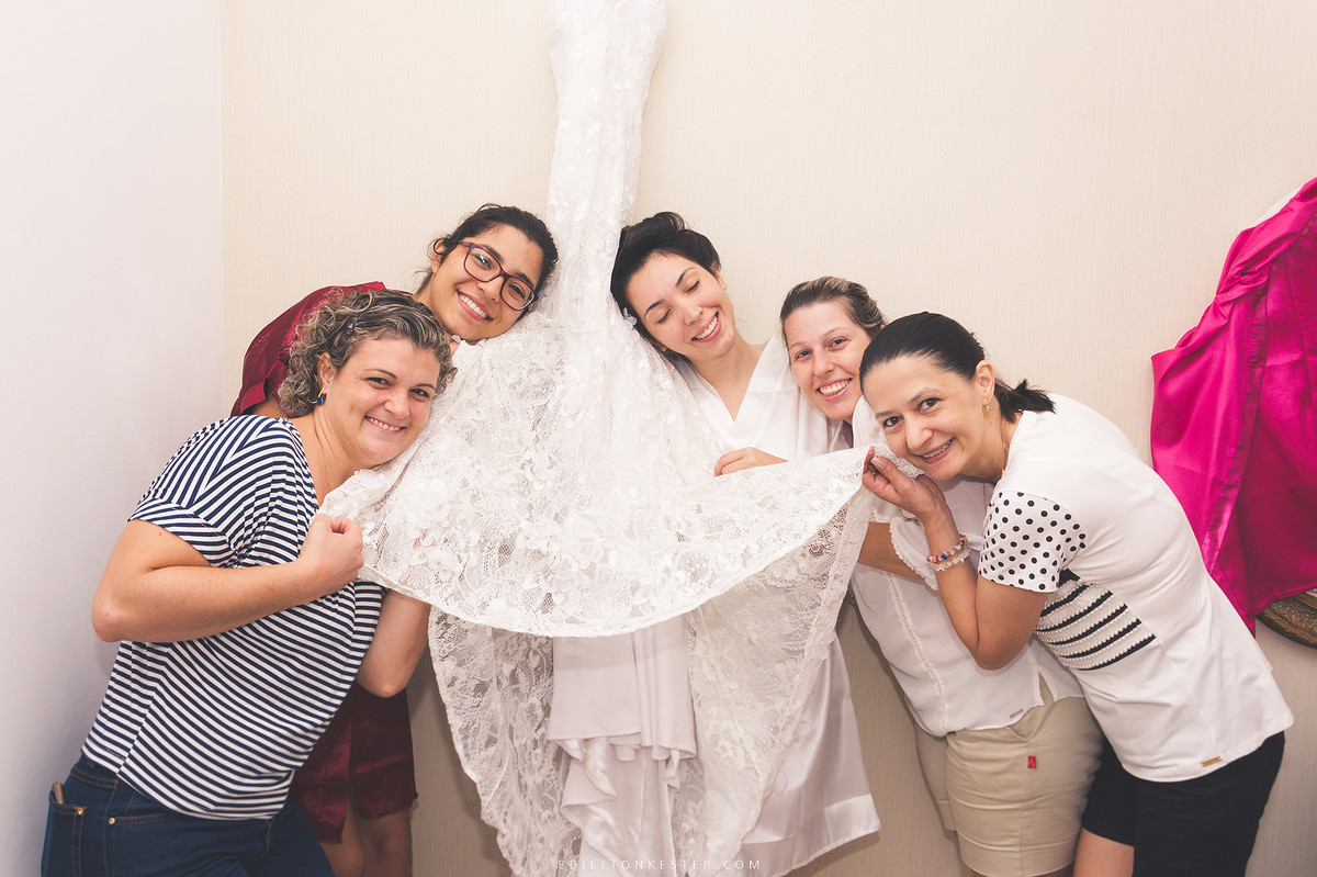 noiva com suas amigas segurando vestido de noiva em salao