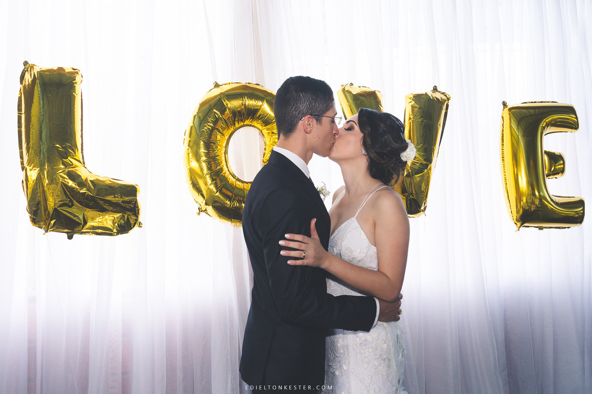 noivos se beijando na recepção posando para fotos com balao de love