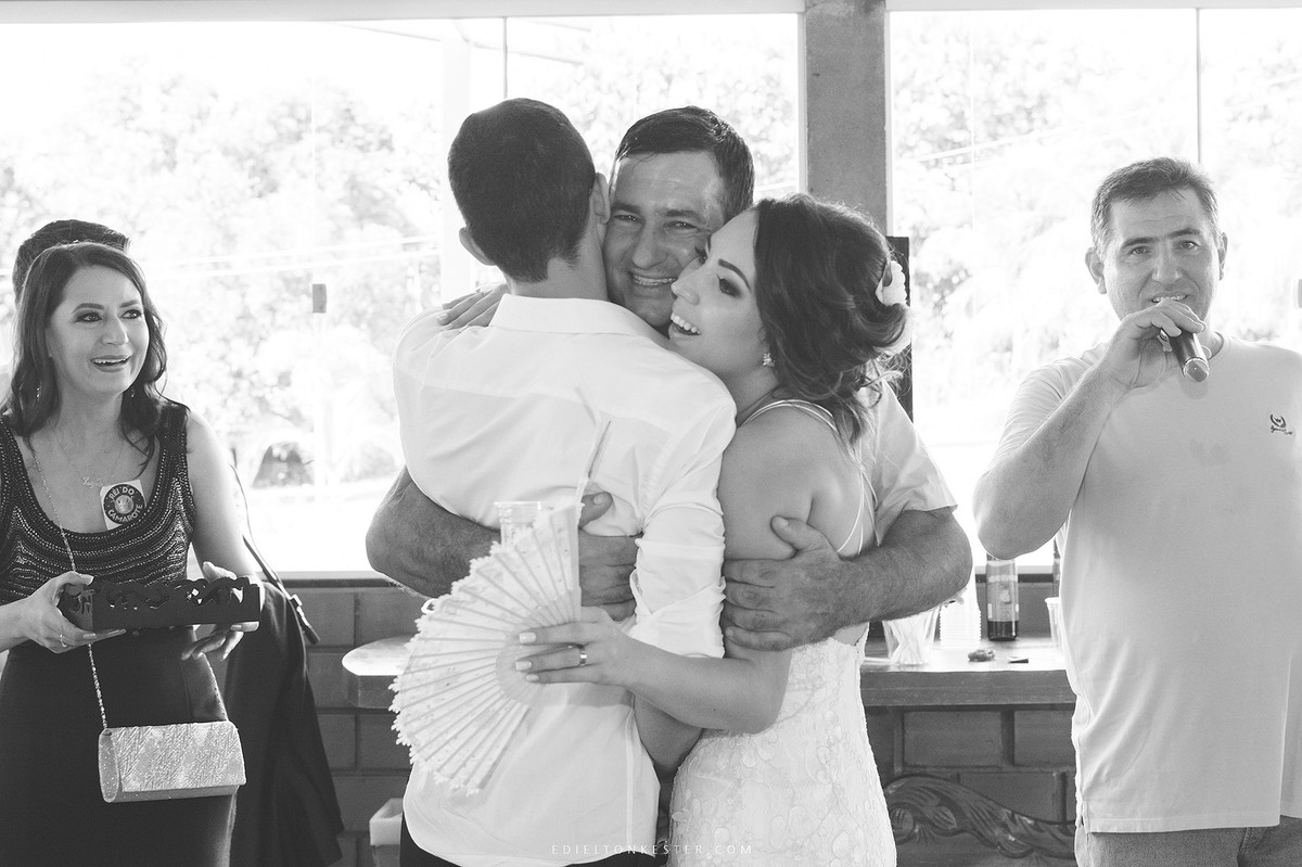 pai do noivo abraçando os recem casados de forma muito carinhosa
